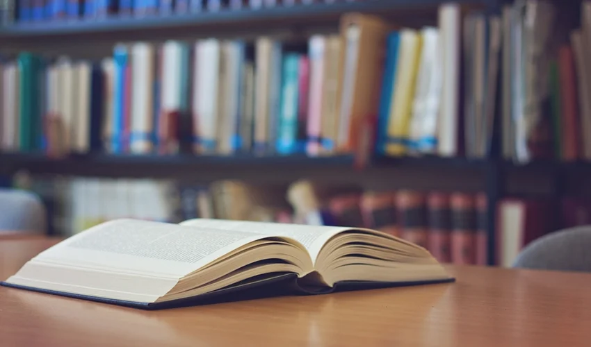 Open book on table in front of library.